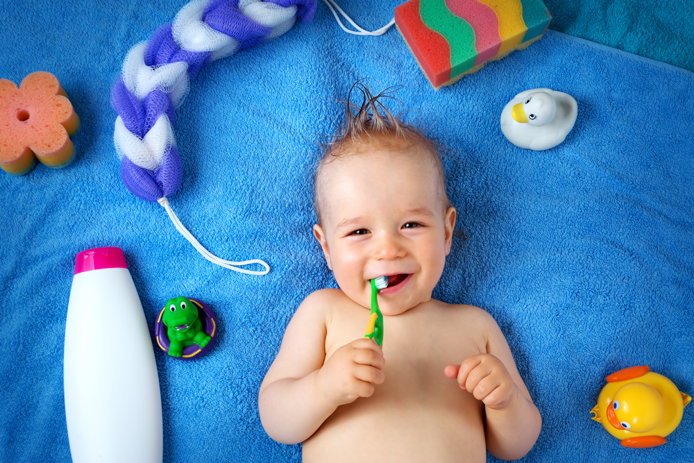 A baby lying on a blue towel with a toothbrush in his mouth.