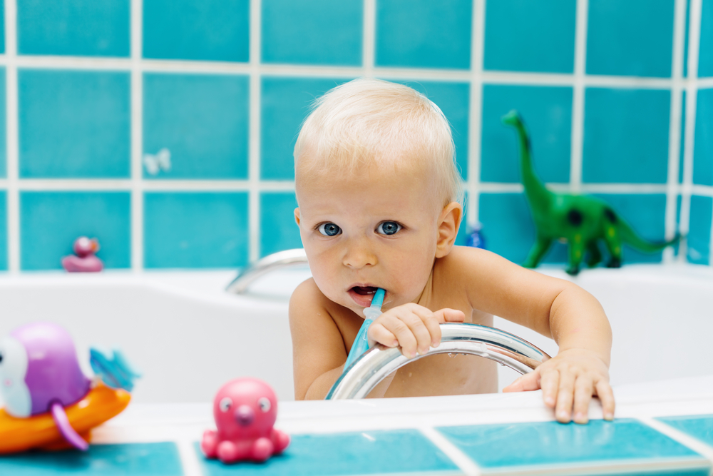 A baby is brushing his teeth in the bathtub.