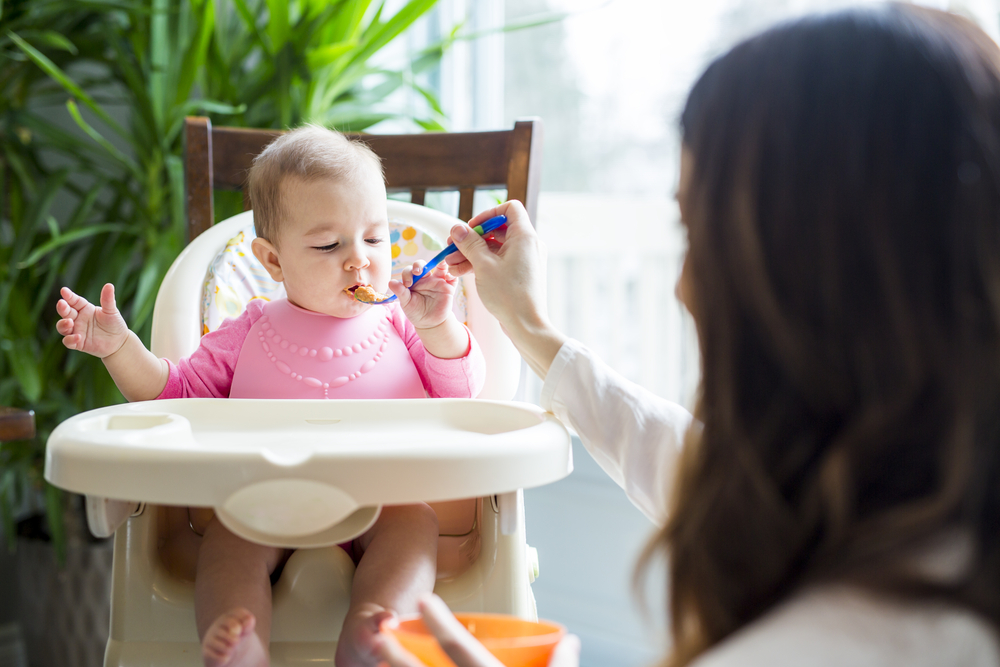 A woman feeding a baby in a high chair.