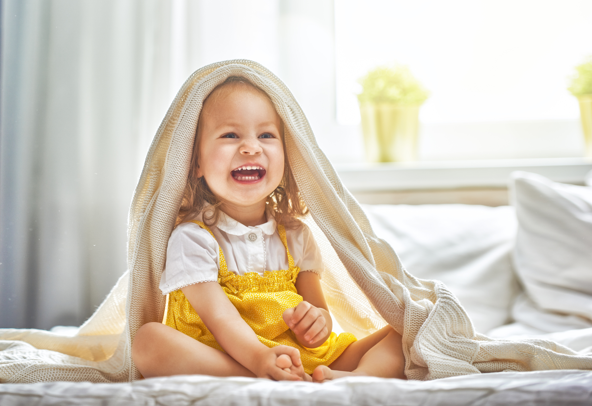 A little girl is sitting under a blanket on a bed.