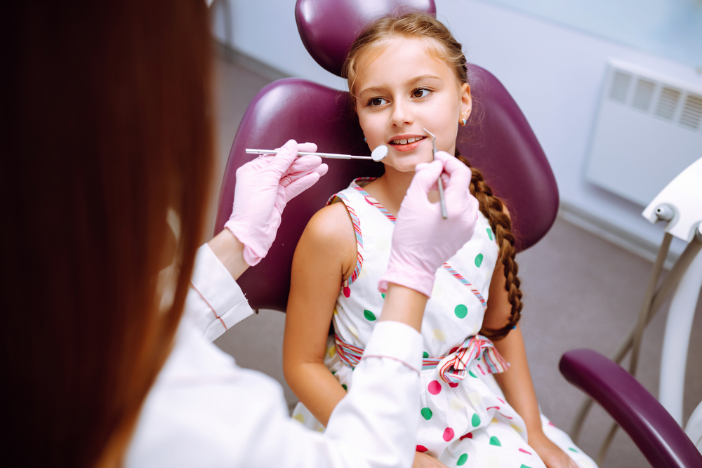 A young girl is getting her teeth checked by a dentist.