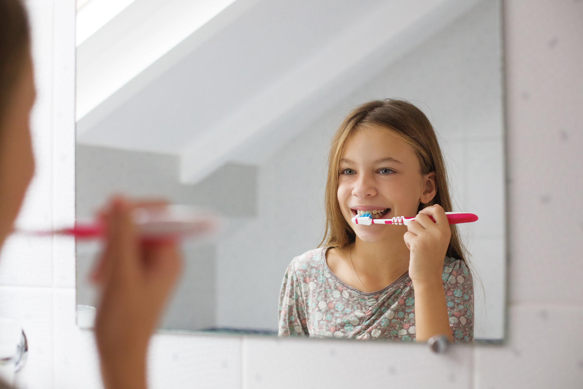 A girl brushing her teeth in front of a mirror.