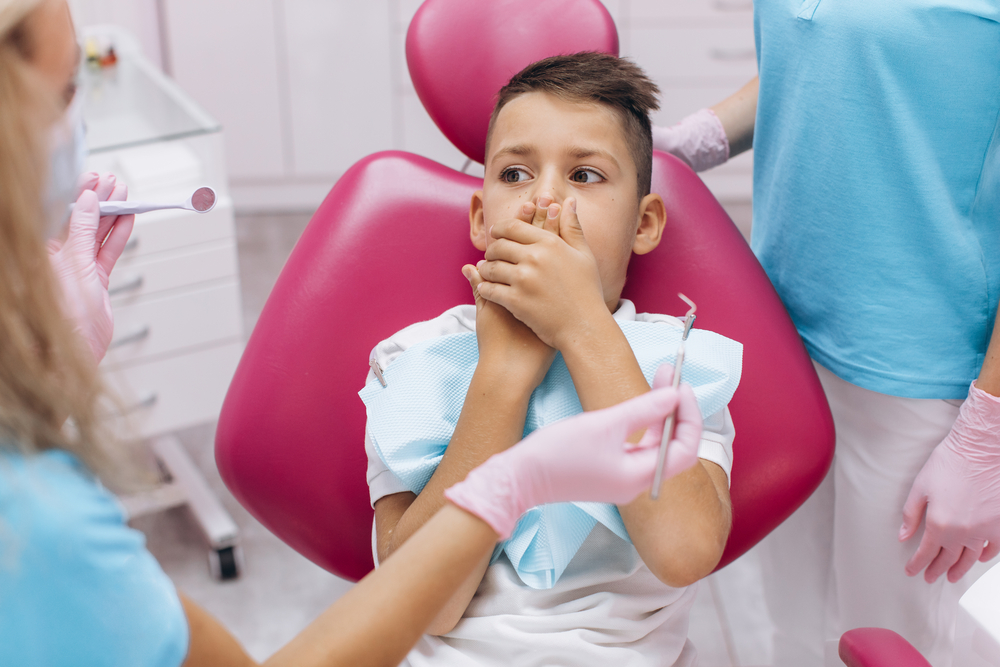 The boy is scared and closes his mouth with his hands on a visit A young boy is sitting in a dentist's chair.