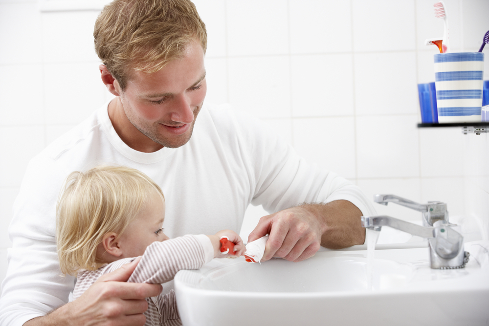 A man is brushing his child's teeth in the bathroom.
