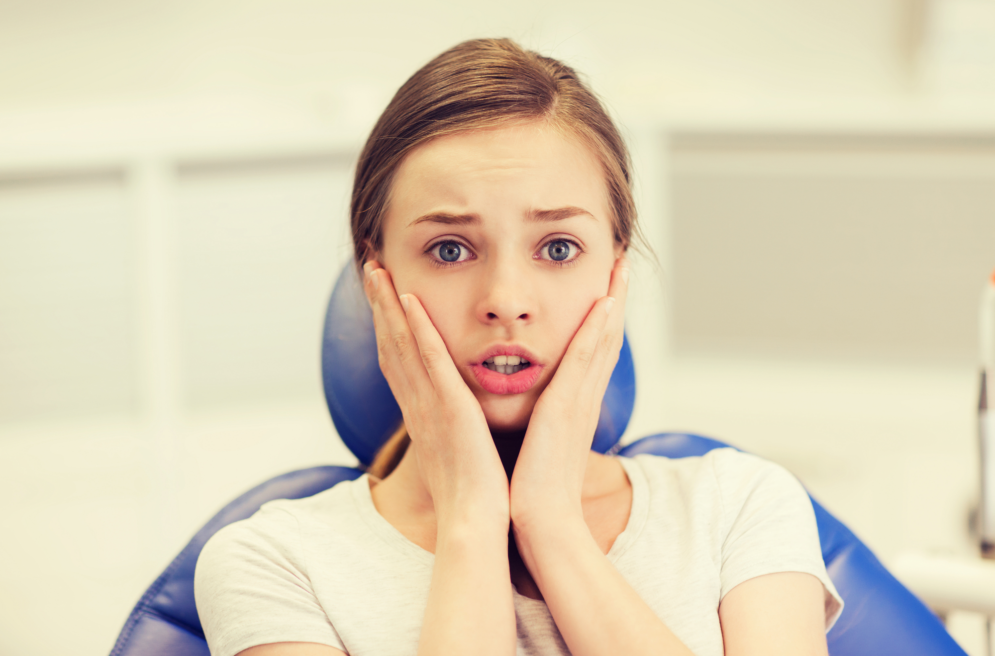 A woman sitting in a dentist chair with her hands on her face.