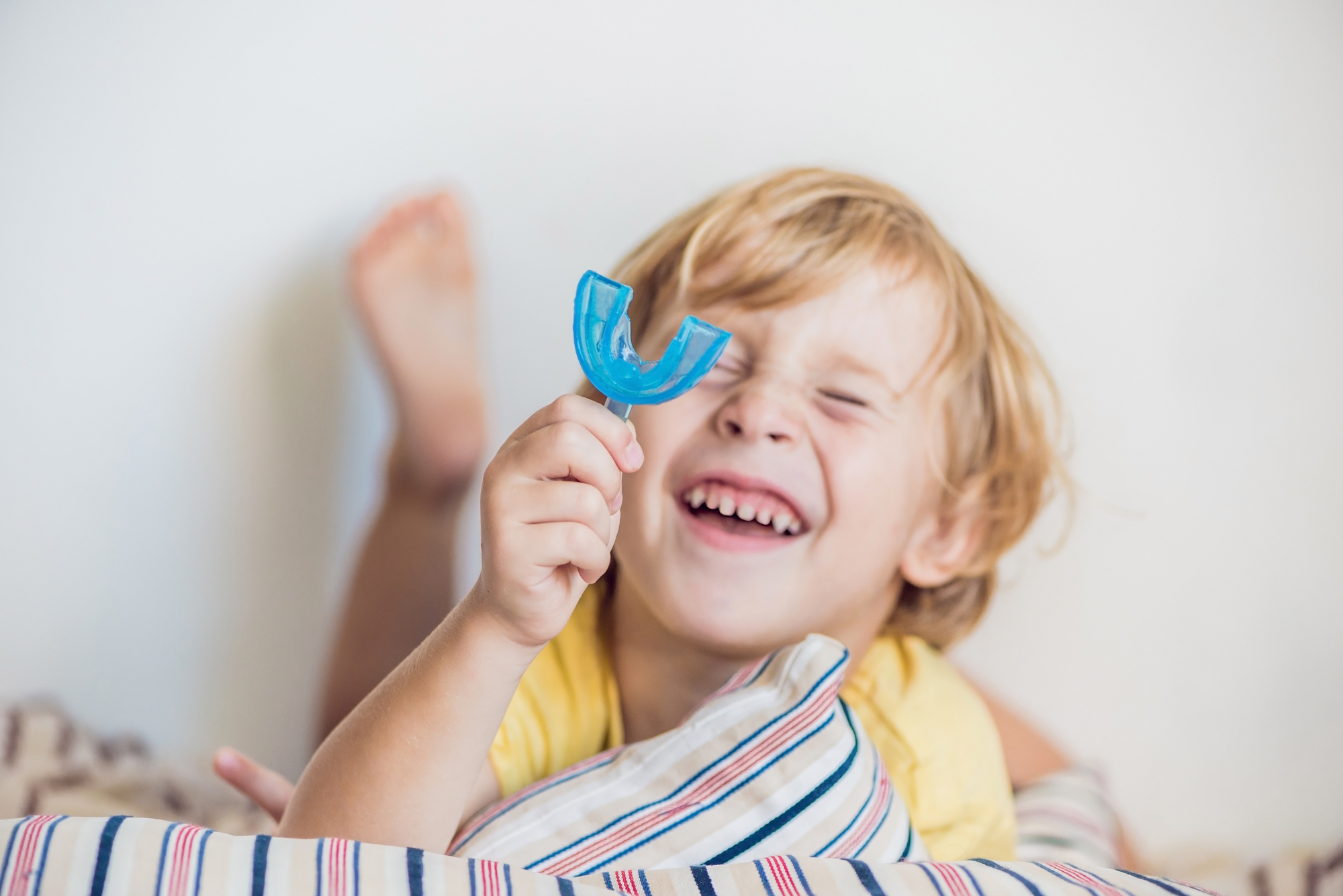 A young boy laying on a bed with a blue toothpick in his mouth.